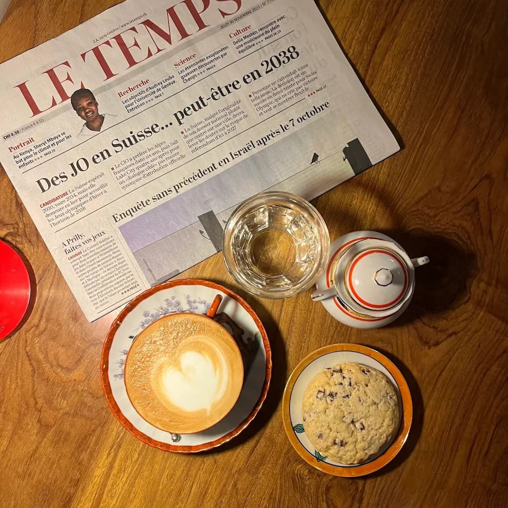 Un café, un cookie et le journal Le Temps posés sur une table en bois du Café Le Passage, à Genève.