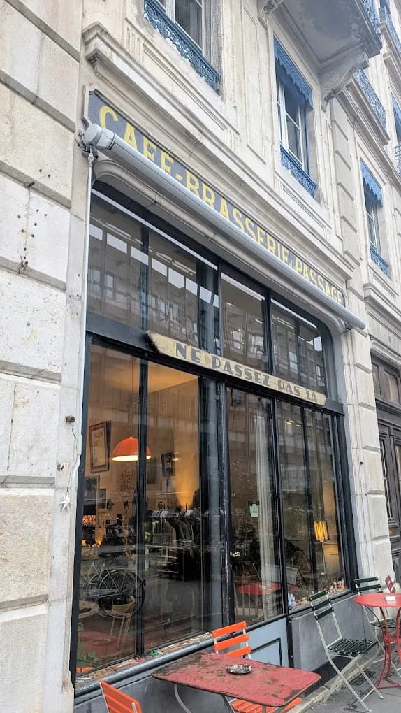 La devanture du Café-Brasserie Le Passage, son enseigne émaillée jaune et ses chaises bistrot, rue des Gares à Genève.
