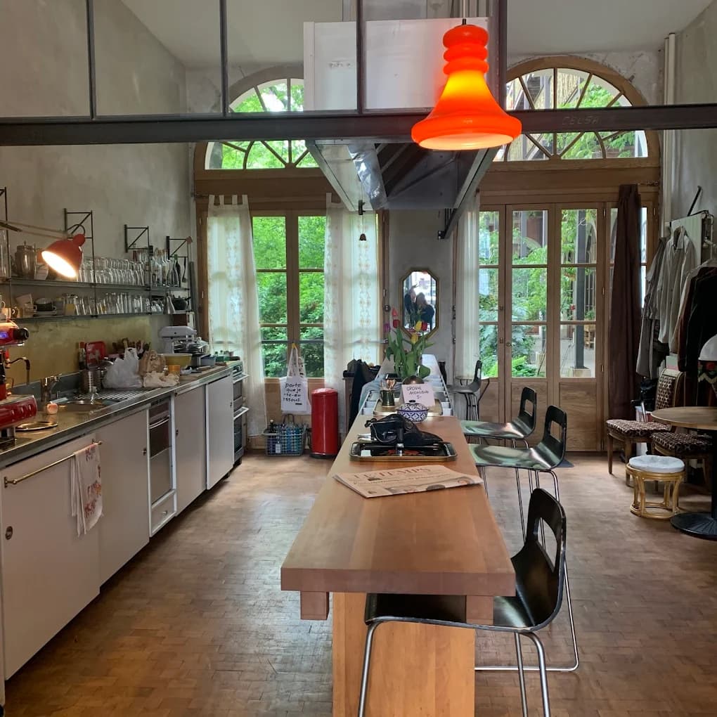 L'atelier du Café Le Passage : verrières en arc, bar en bois, lampes oranges et mobilier chiné, à Genève.