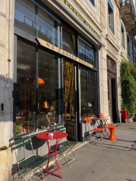 La terrasse du Café Le Passage : tables rouges et chaises bistrot vertes et oranges sur le trottoir de la rue des Gares, Genève.